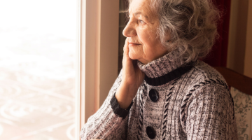 elderly woman sitting at a window with a cup of tea