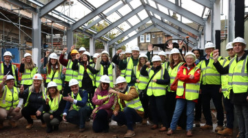 Group photo of people in hi-vis jackets on a building site holding up pens