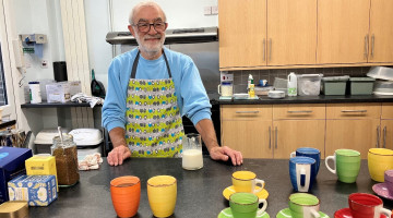 A photo showing a smiling man who is making hot drinks in a kitchen