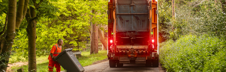 A man collecting a bin in a wooded area next to a bin lorry