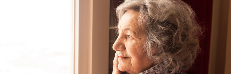 elderly woman sitting at a window with a cup of tea