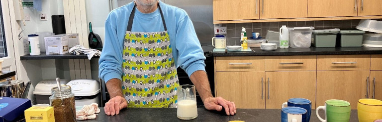 A photo showing a smiling man who is making hot drinks in a kitchen